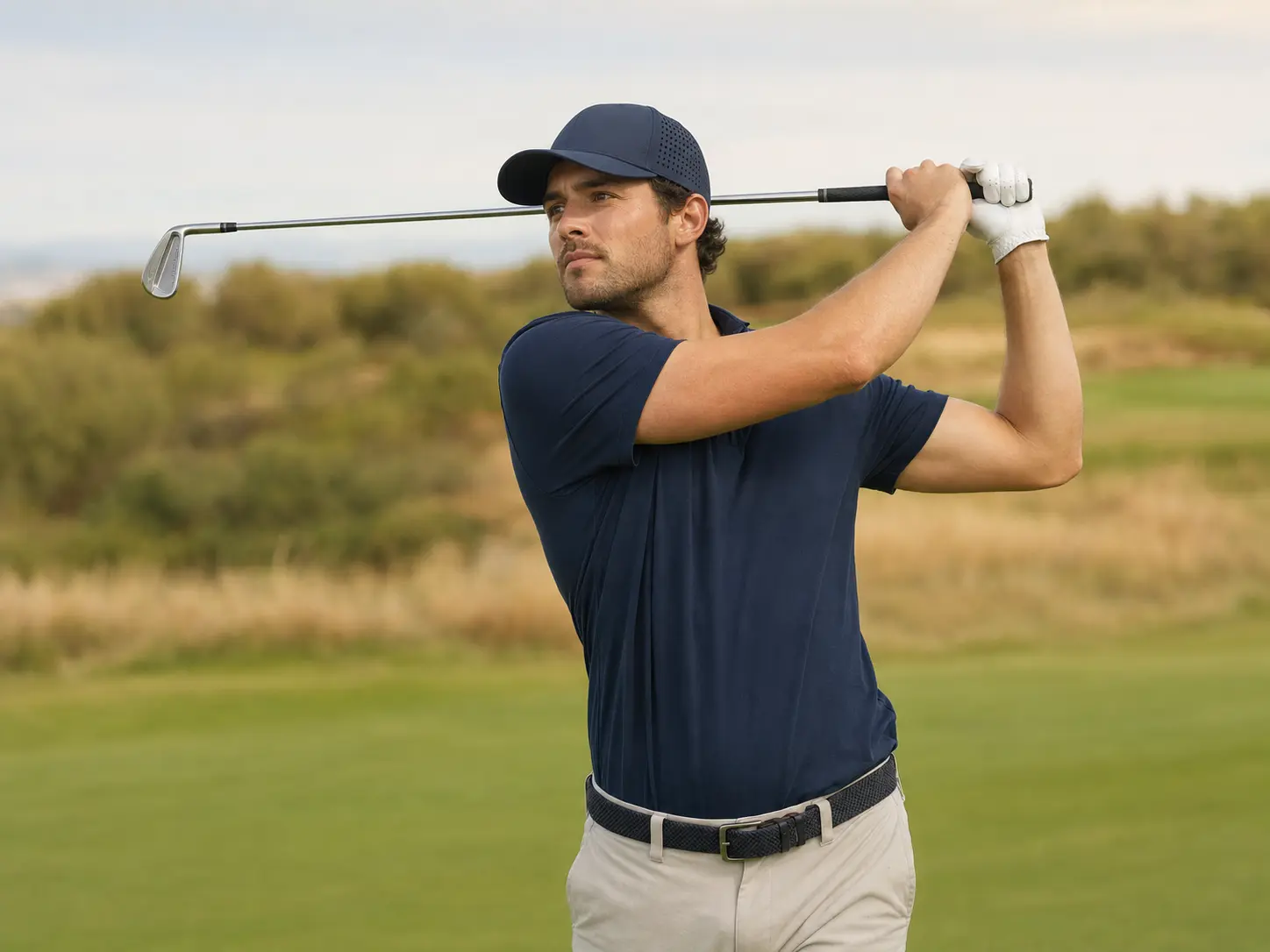 Golfer finishing a golf swing in a navy laser-perforated performance cap