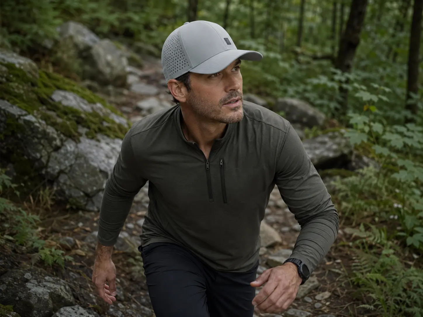Hiker climbing a wet forest trail in a grey laser-perforated performance cap